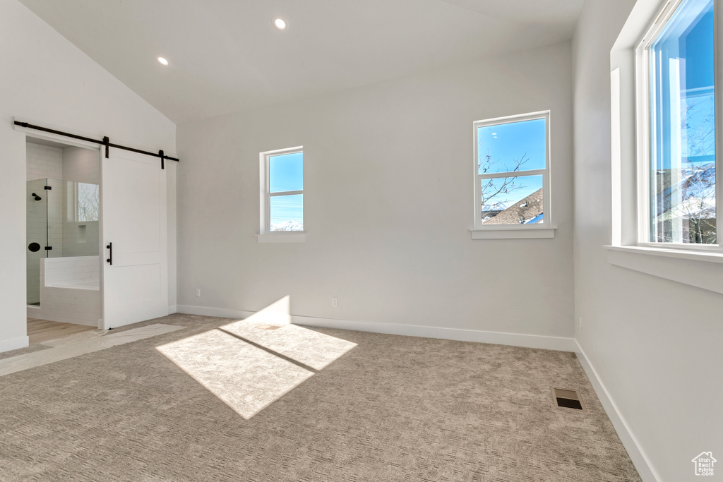 Unfurnished bedroom featuring lofted ceiling, light carpet, and a barn door