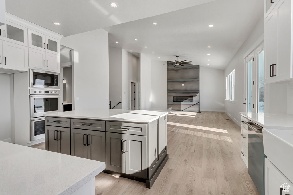 Kitchen featuring a center island, light hardwood / wood-style flooring, white cabinetry, black microwave, and ceiling fan