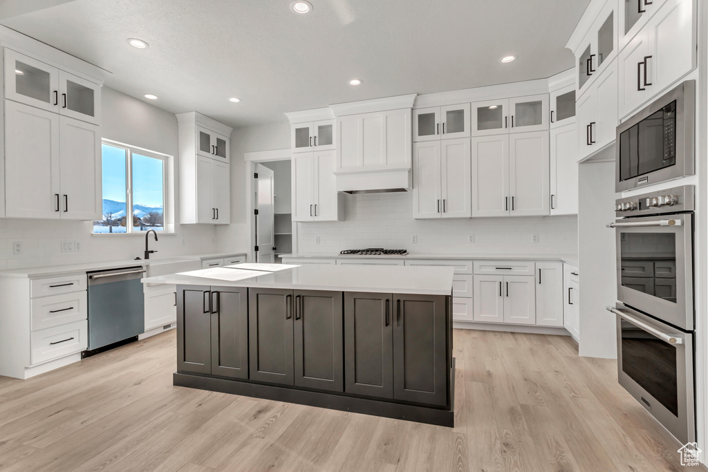 Kitchen featuring a kitchen island, light wood-type flooring, white cabinetry, and stainless steel appliances