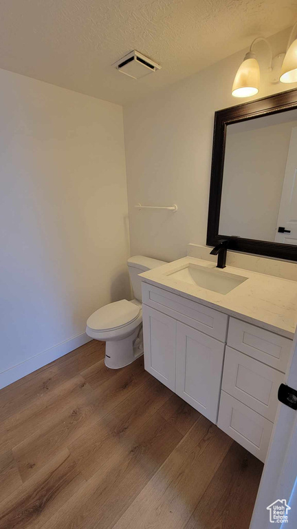 Bathroom with vanity with extensive cabinet space, hardwood / wood-style flooring, toilet, and a textured ceiling