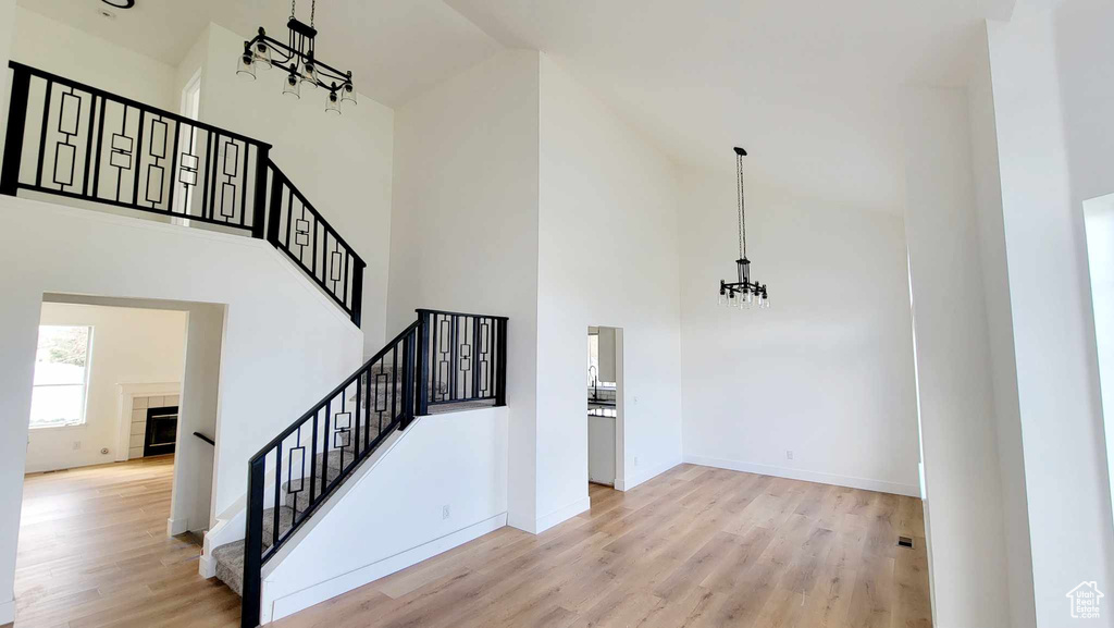 Staircase featuring light hardwood / wood-style flooring, a towering ceiling, an inviting chandelier, and a tiled fireplace