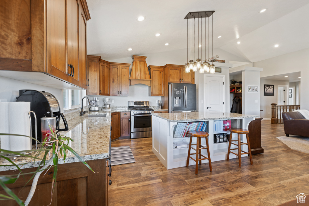 Kitchen with dark wood-type flooring, appliances with stainless steel finishes, a kitchen island, light stone countertops, and hanging light fixtures