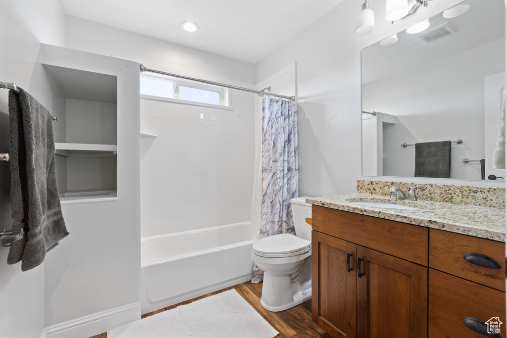 Full bathroom featuring hardwood / wood-style floors, shower / bath combo with shower curtain, toilet, and vanity
