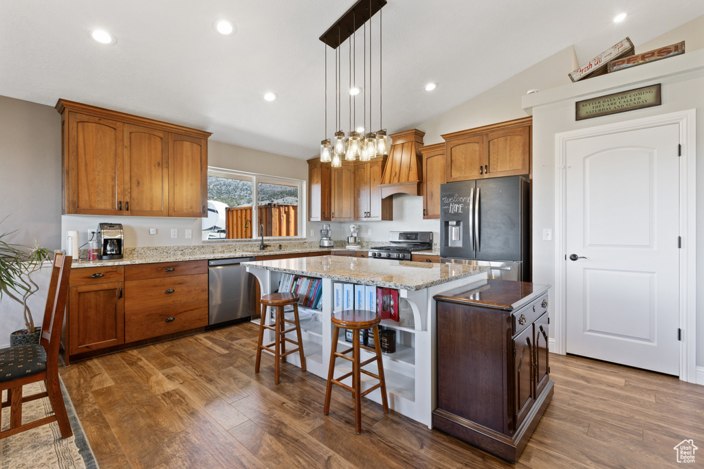 Kitchen featuring dark hardwood / wood-style flooring, decorative light fixtures, stainless steel appliances, a center island, and lofted ceiling