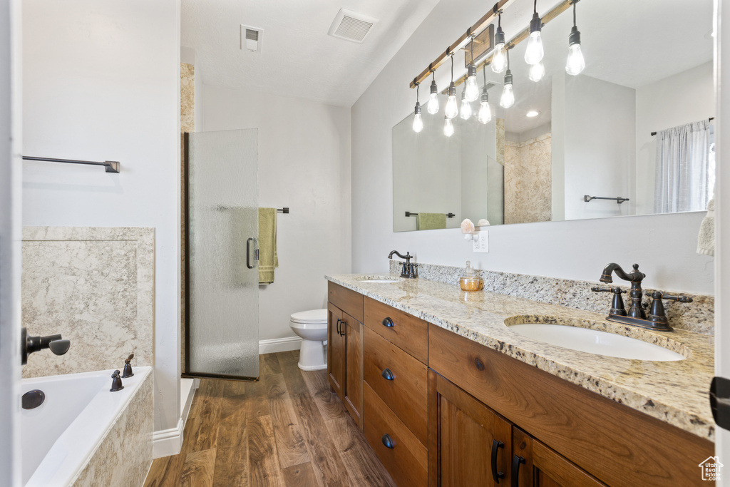 Full bathroom featuring toilet, large vanity, double sink, wood-type flooring, and shower with separate bathtub