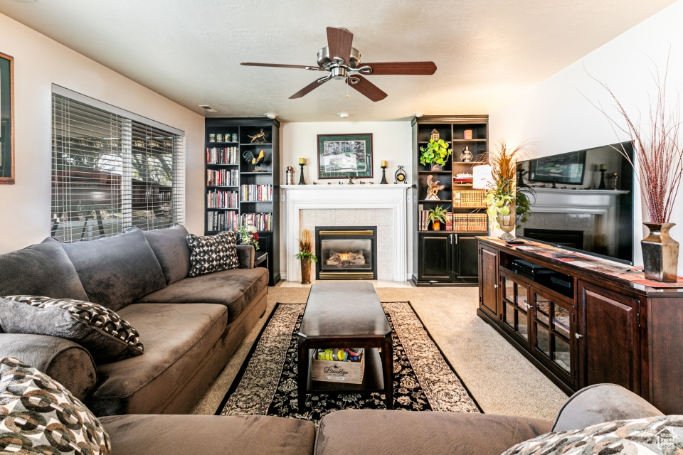 Carpeted living room featuring ceiling fan, a fireplace, and built in shelves