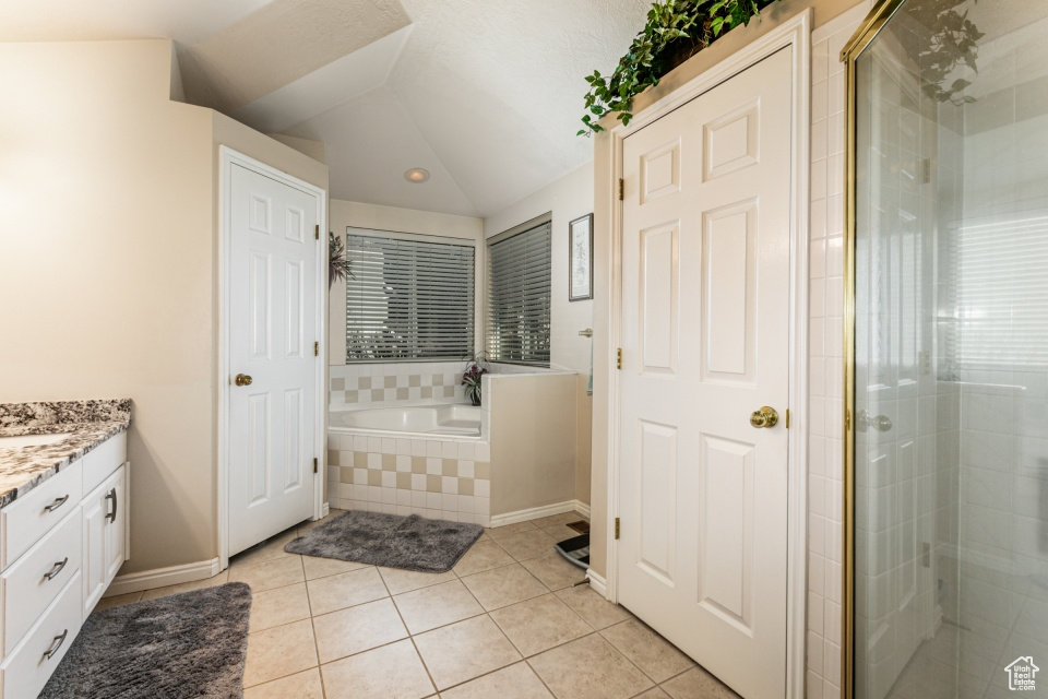 Bathroom featuring separate shower and tub, tile floors, vanity, and vaulted ceiling