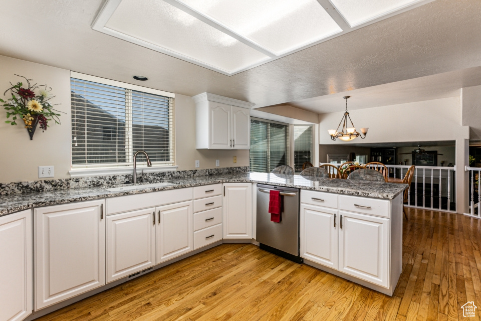 Kitchen with white cabinets, light wood-type flooring, kitchen peninsula, sink, and dishwasher