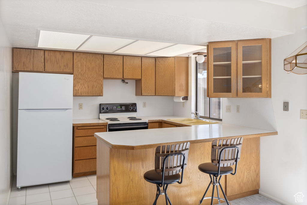 Kitchen featuring white appliances, kitchen peninsula, light tile floors, sink, and a breakfast bar area