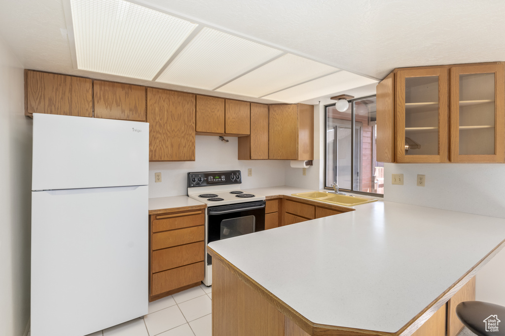 Kitchen featuring light tile floors, kitchen peninsula, white appliances, and sink