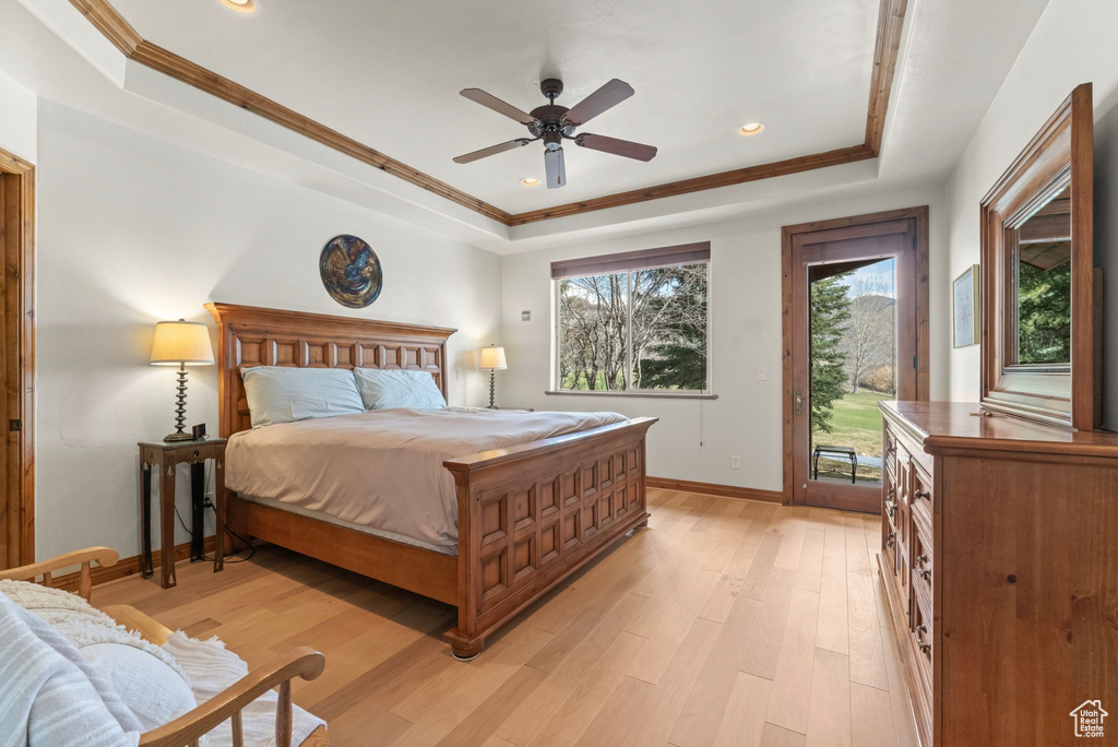 Bedroom with ceiling fan, access to exterior, light wood-type flooring, and a tray ceiling