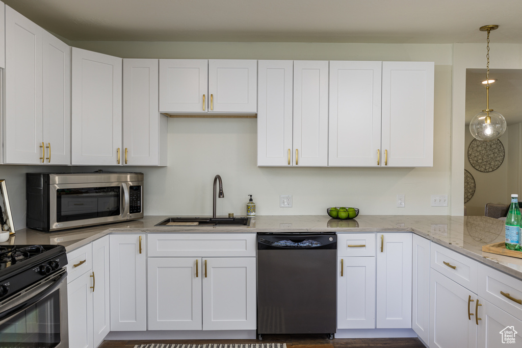 Kitchen featuring light stone countertops, dishwashing machine, white cabinetry, sink, and pendant lighting