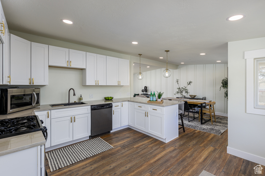 Kitchen featuring appliances with stainless steel finishes, dark hardwood / wood-style flooring, white cabinets, sink, and pendant lighting