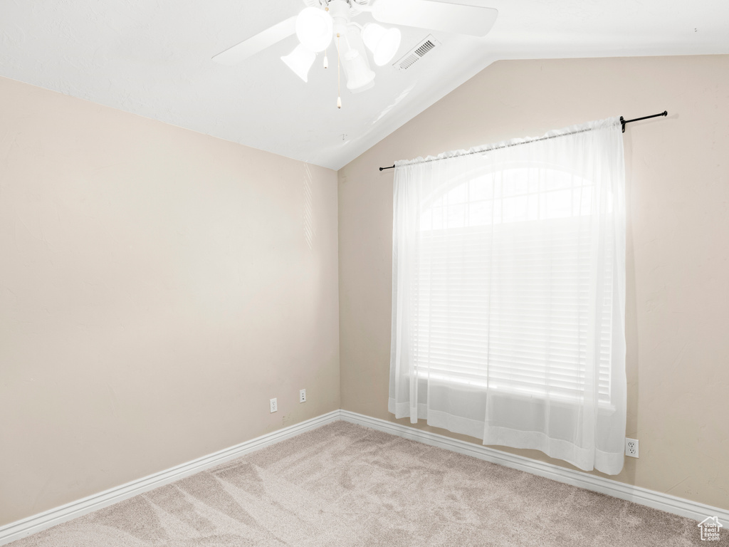 Carpeted empty room featuring a healthy amount of sunlight, ceiling fan, and vaulted ceiling