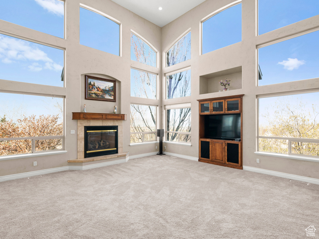 Unfurnished living room featuring light colored carpet, a wealth of natural light, and a tile fireplace