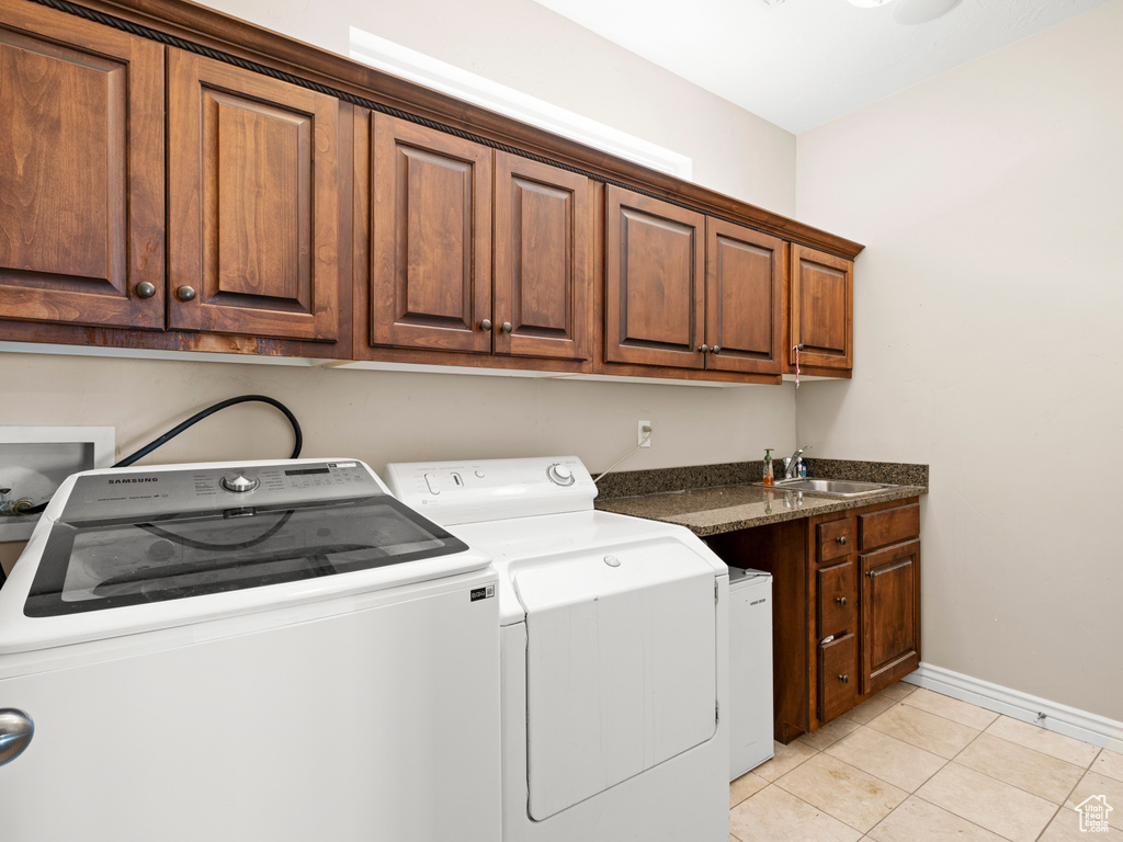 Washroom with cabinets, light tile floors, washing machine and clothes dryer, sink, and hookup for a washing machine