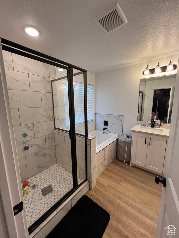 Bathroom with vanity with extensive cabinet space, shower with separate bathtub, hardwood / wood-style flooring, and a textured ceiling