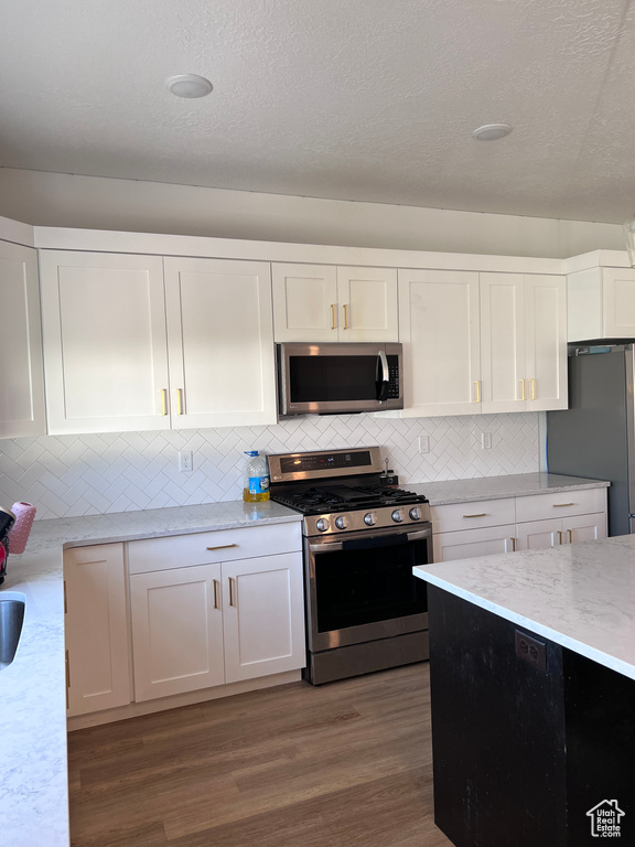 Kitchen featuring tasteful backsplash, stainless steel appliances, hardwood / wood-style flooring, and white cabinetry