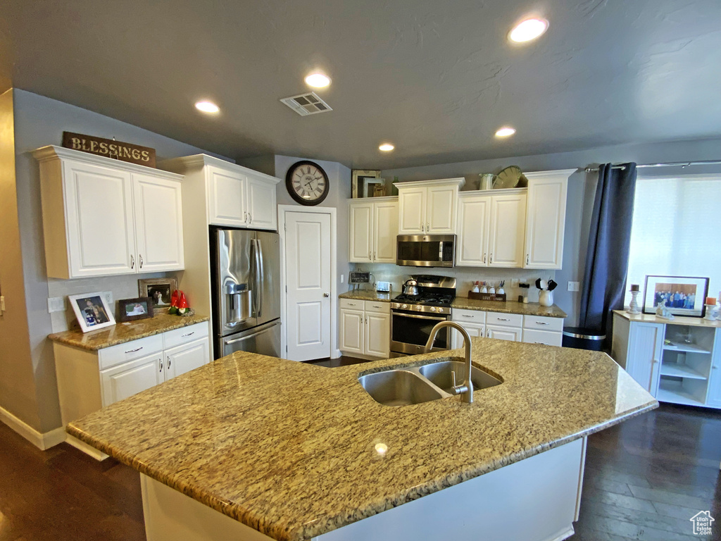 Kitchen featuring appliances with stainless steel finishes, white cabinetry, and a center island with sink