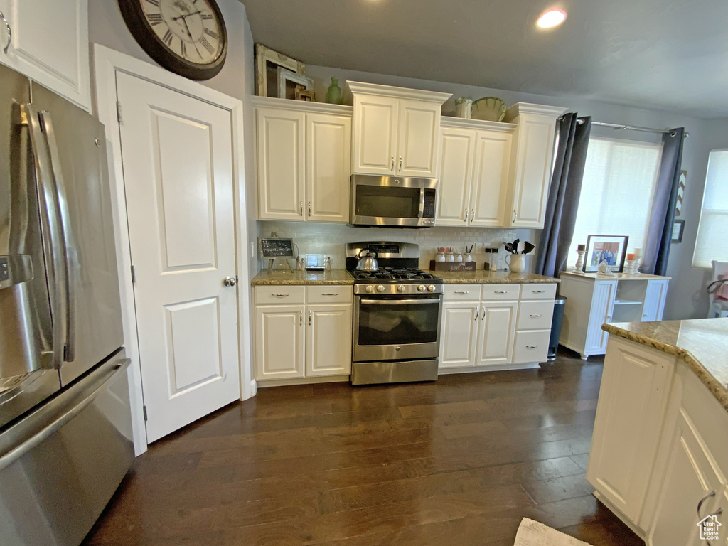 Kitchen with light stone countertops, stainless steel appliances, dark hardwood / wood-style floors, tasteful backsplash, and white cabinets