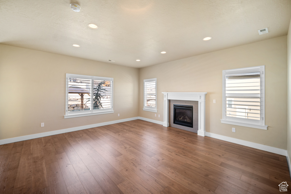 Unfurnished living room featuring a brick fireplace and dark hardwood / wood-style floors