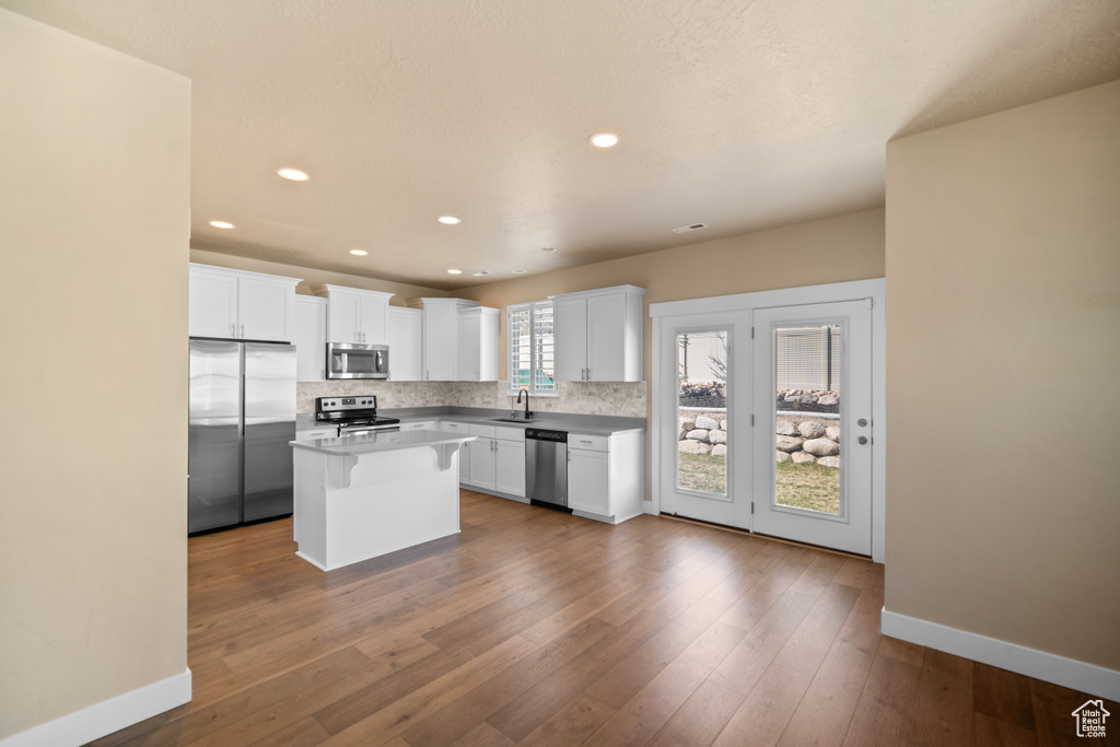 Kitchen featuring hardwood / wood-style floors, a kitchen island, white cabinetry, and stainless steel appliances