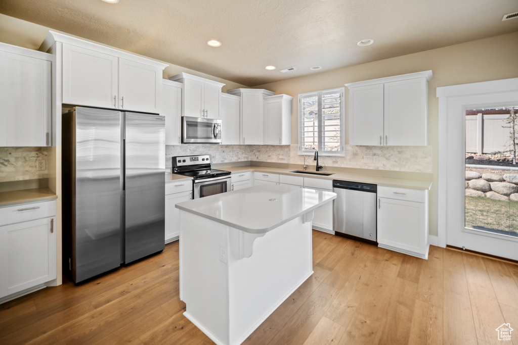Kitchen with appliances with stainless steel finishes, light hardwood / wood-style floors, and white cabinets