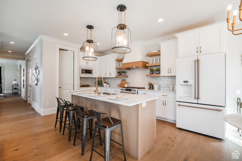 Kitchen featuring white cabinets, stainless steel appliances, light wood-type flooring, and an island with sink