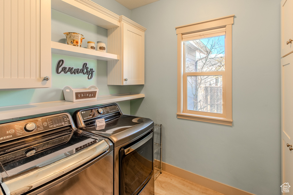 Laundry area with independent washer and dryer, light hardwood / wood-style floors, and cabinets