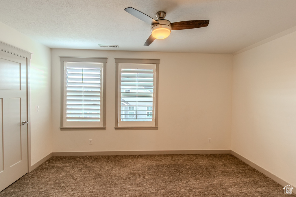Spare room featuring ceiling fan and dark colored carpet