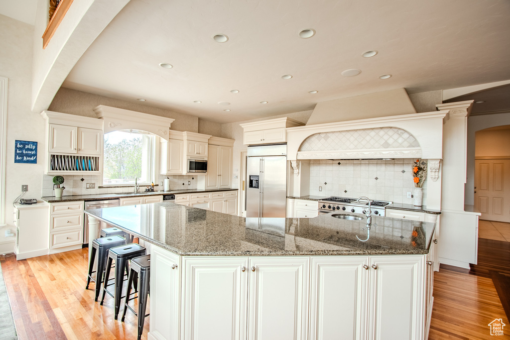 Kitchen with white cabinets, backsplash, built in appliances, and an island with sink