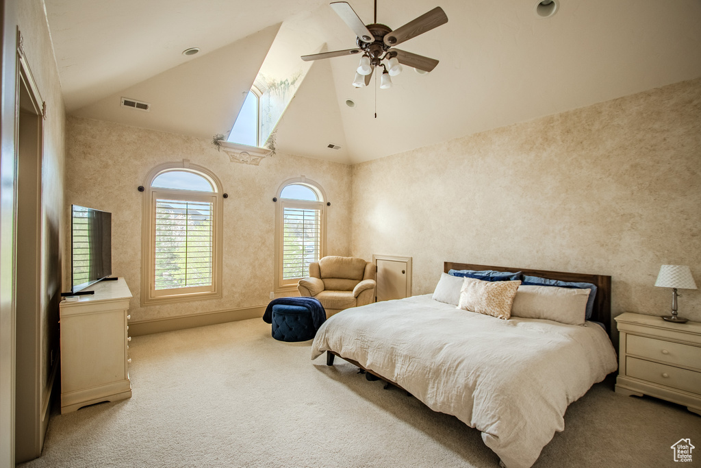 Bedroom with light colored carpet, a skylight, ceiling fan, and high vaulted ceiling