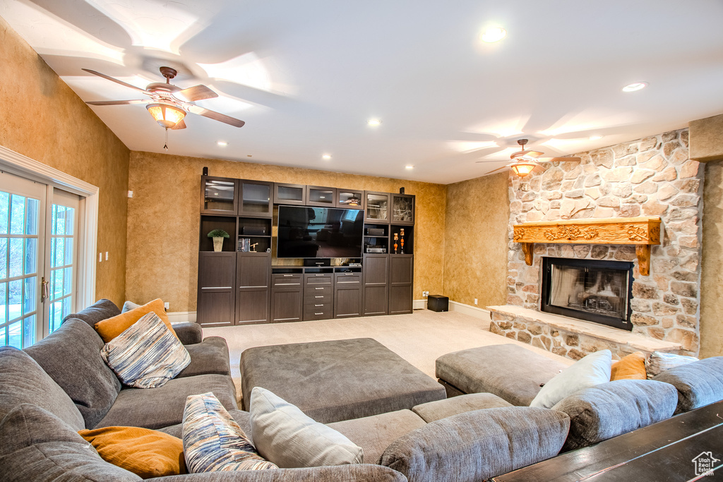 Carpeted living room with a stone fireplace and ceiling fan