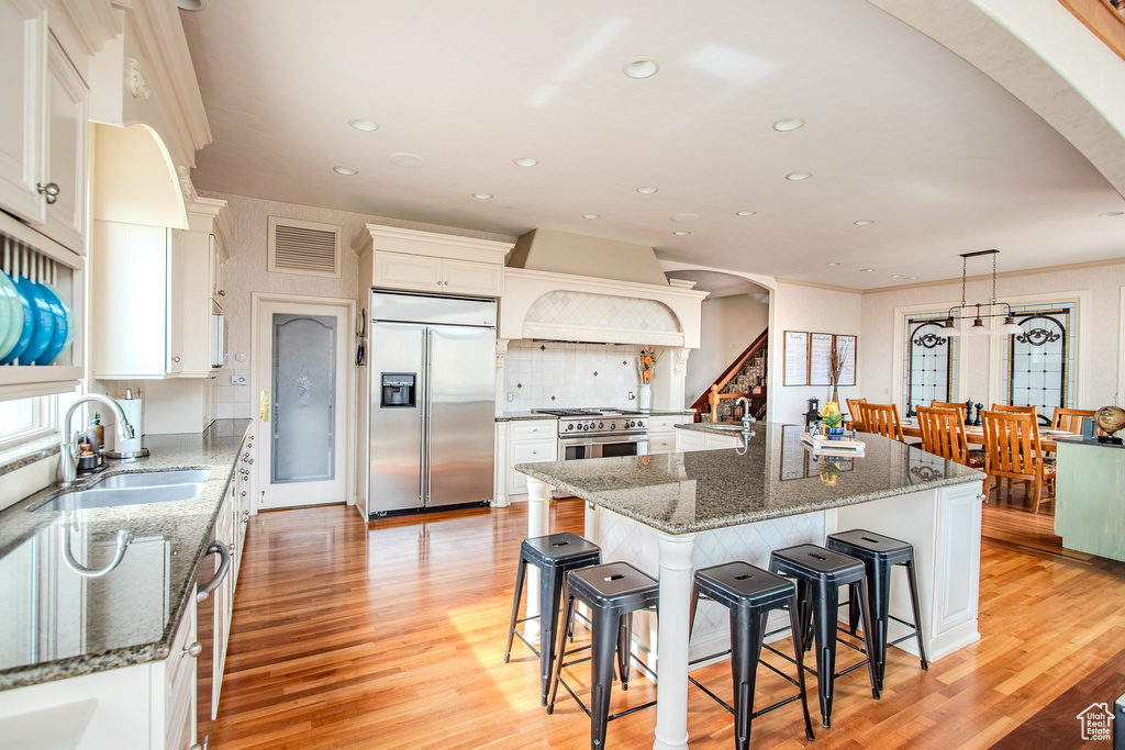 Kitchen featuring light hardwood / wood-style floors, a center island with sink, custom range hood, tasteful backsplash, and high quality appliances