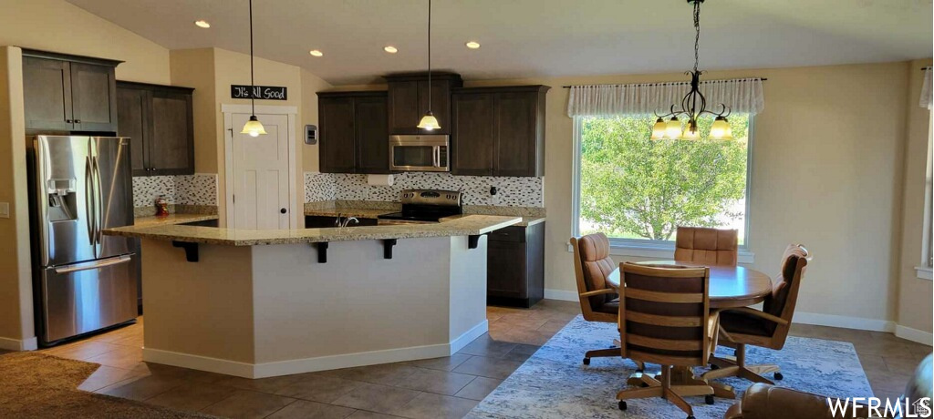 Kitchen with tasteful backsplash, appliances with stainless steel finishes, hanging light fixtures, and vaulted ceiling