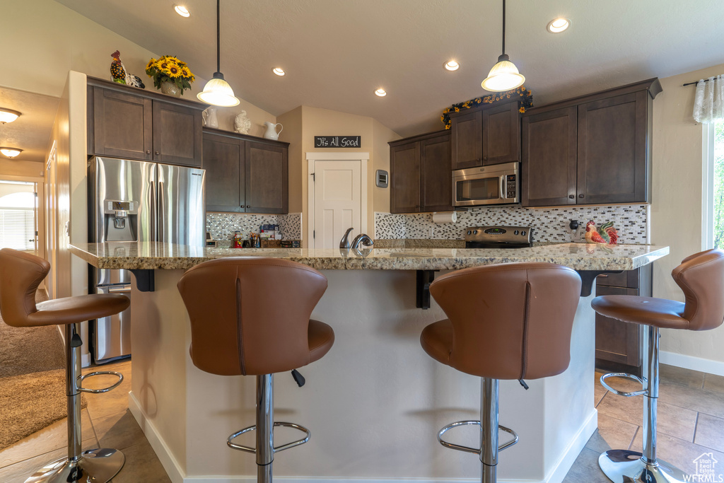 Kitchen with appliances with stainless steel finishes, backsplash, light tile floors, and a kitchen breakfast bar