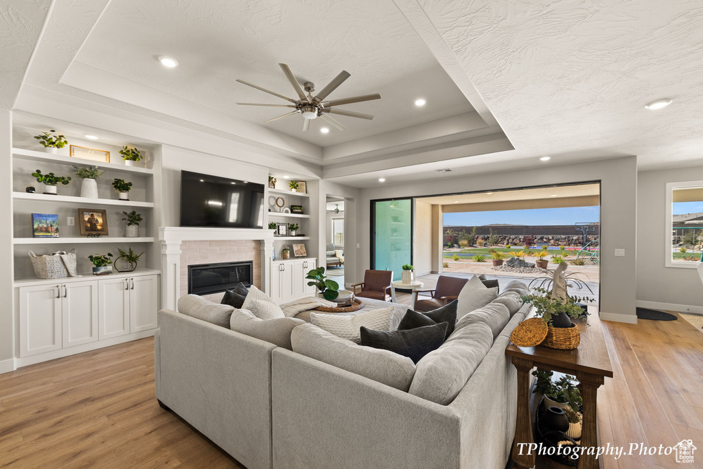 Living room with built in features, ceiling fan, a textured ceiling, a tray ceiling, and light wood-type flooring