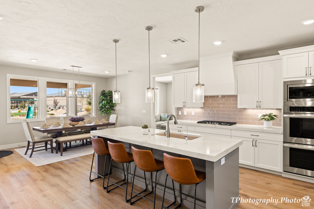 Kitchen featuring decorative light fixtures, tasteful backsplash, white cabinets, sink, and light wood-type flooring