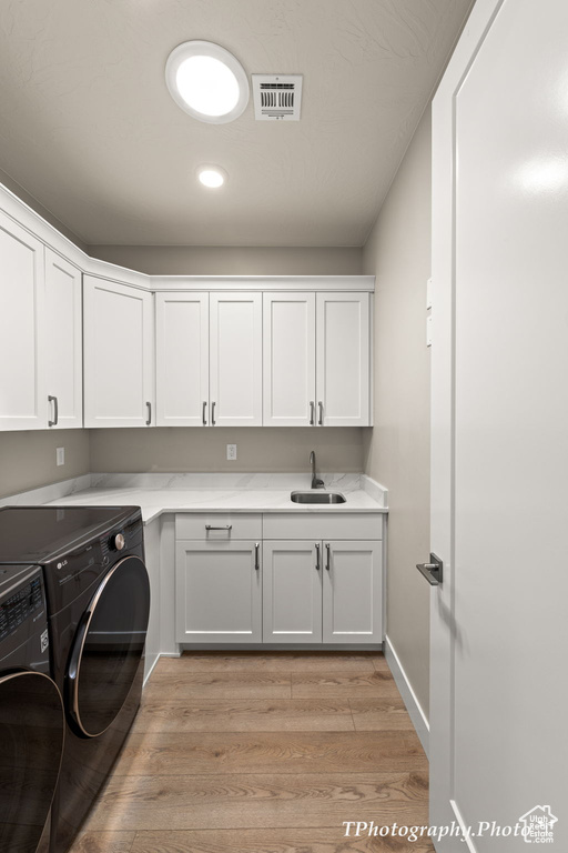 Washroom featuring washer and clothes dryer, light hardwood / wood-style floors, cabinets, and sink