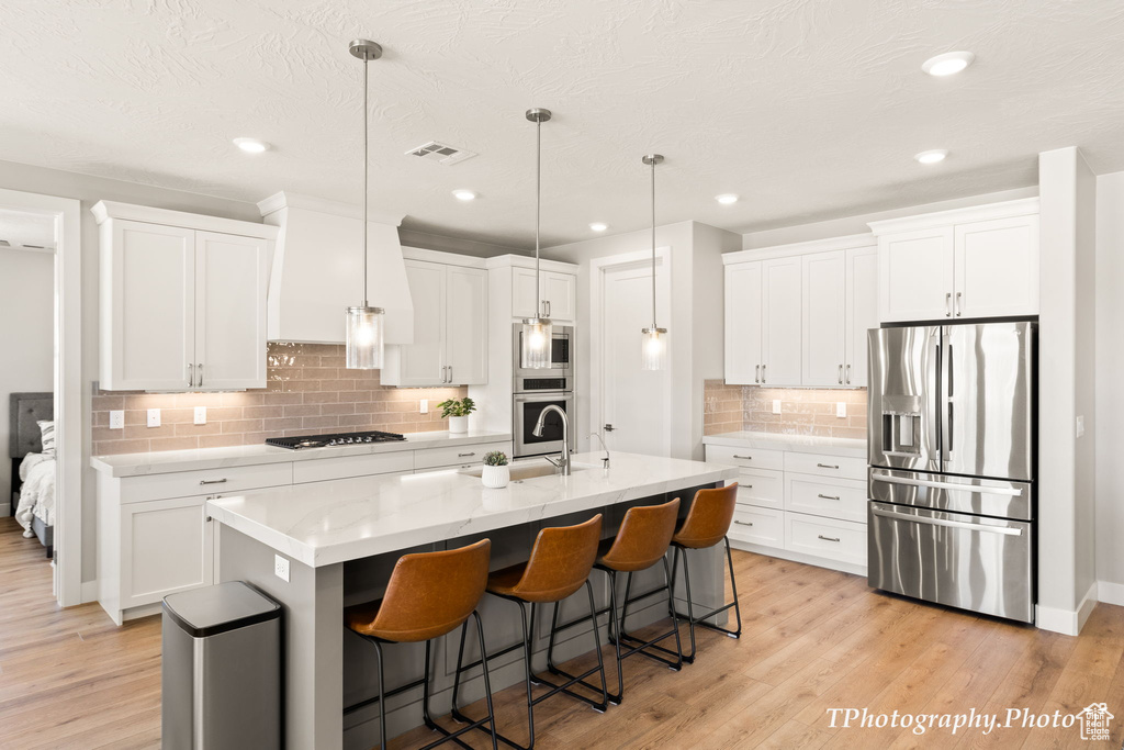 Kitchen with hanging light fixtures, light hardwood / wood-style flooring, stainless steel appliances, tasteful backsplash, and white cabinetry