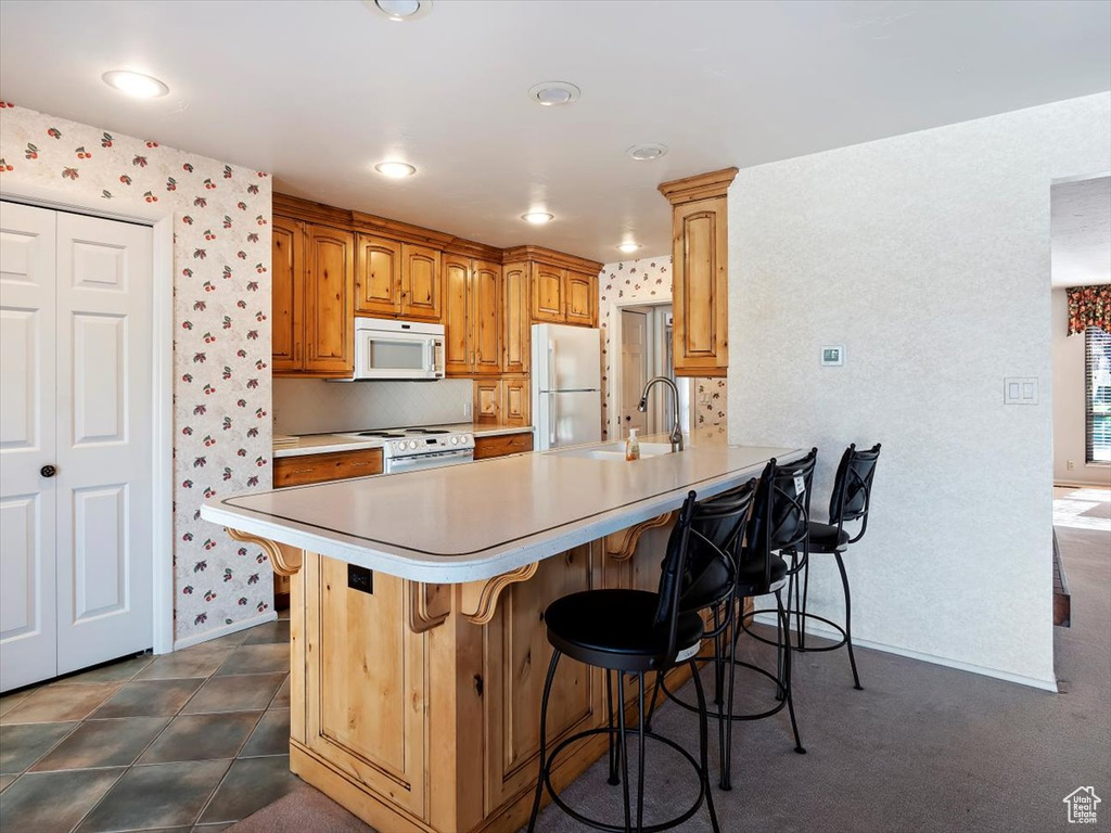 Kitchen with kitchen peninsula, white appliances, dark tile flooring, a kitchen breakfast bar, and sink