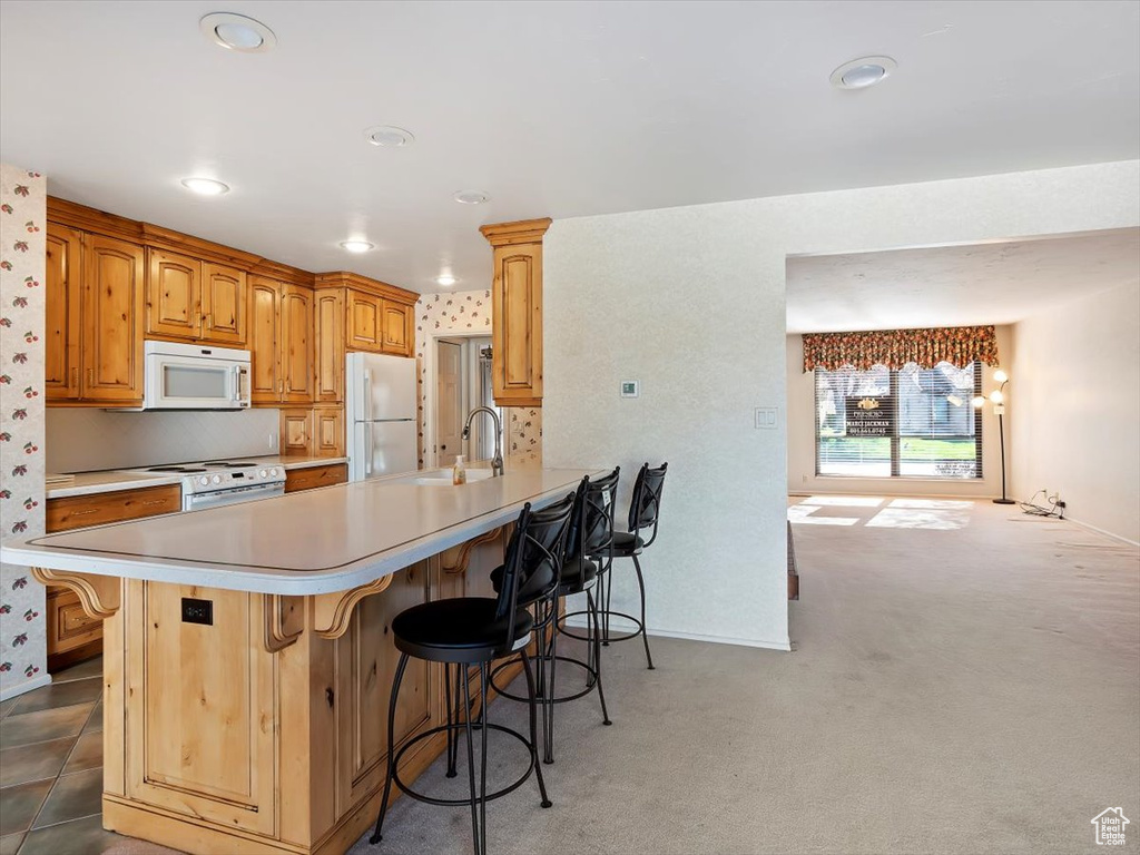 Kitchen featuring white appliances, dark colored carpet, kitchen peninsula, sink, and a breakfast bar area
