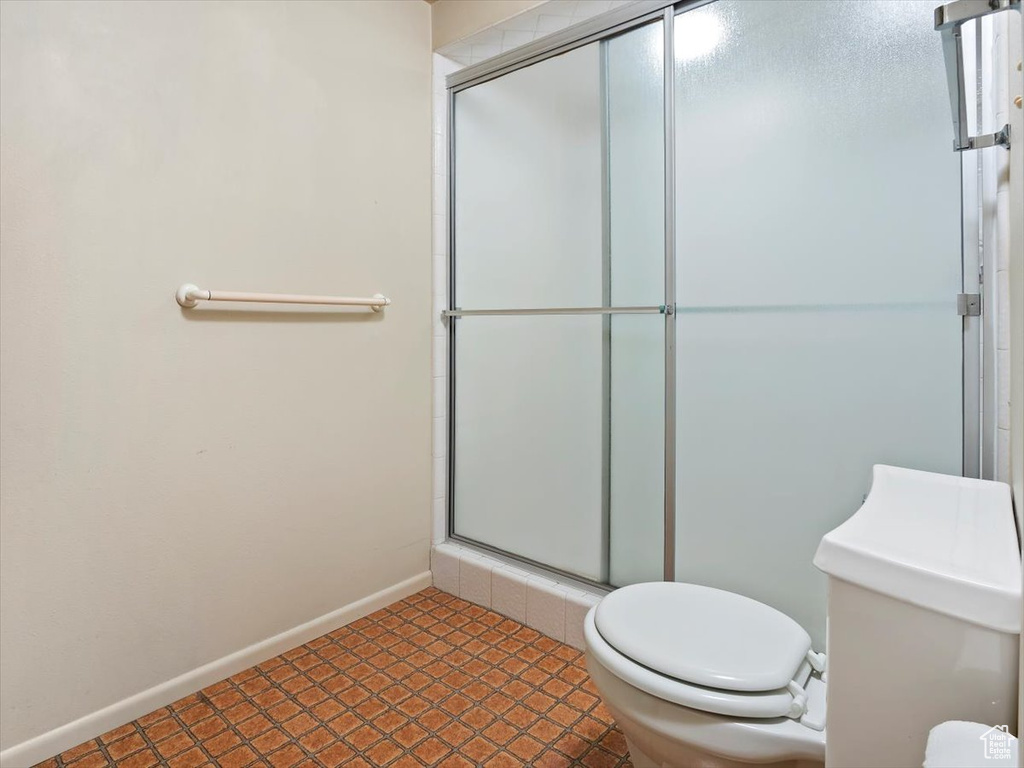 Bathroom featuring a shower with door, tile floors, and toilet