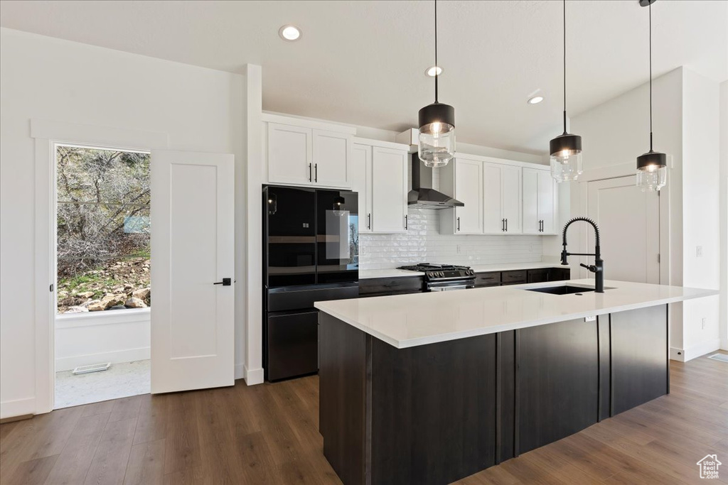 Kitchen featuring stainless steel gas stove, pendant lighting, black refrigerator, and white cabinetry