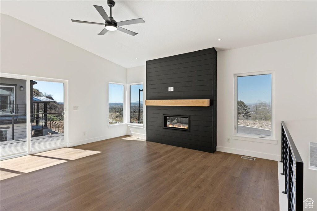 Unfurnished living room featuring a healthy amount of sunlight, ceiling fan, dark hardwood / wood-style floors, and a fireplace