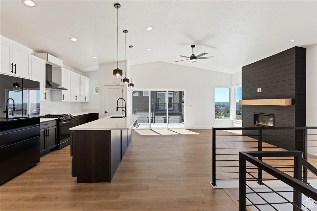 Kitchen with stainless steel range with gas stovetop, a large fireplace, light hardwood / wood-style floors, wall chimney range hood, and pendant lighting