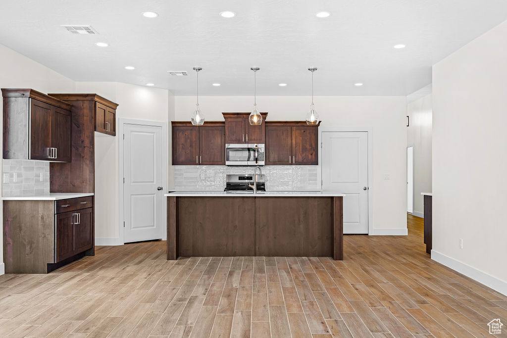 Kitchen featuring pendant lighting, tasteful backsplash, range, dark brown cabinetry, and light hardwood / wood-style flooring