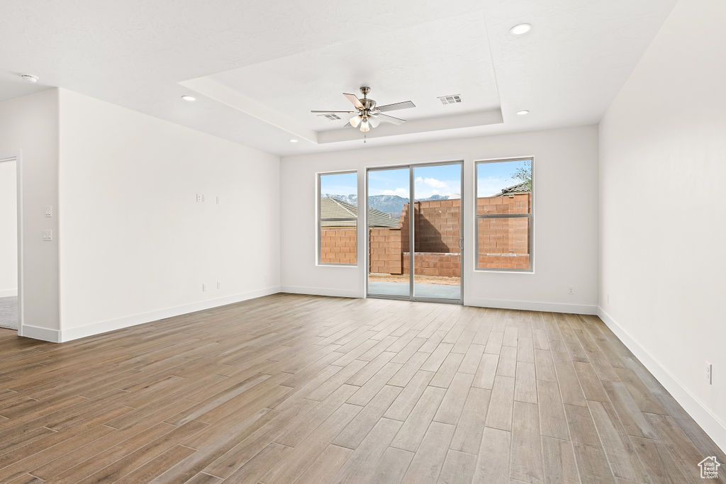 Empty room featuring ceiling fan, a raised ceiling, and light hardwood / wood-style flooring