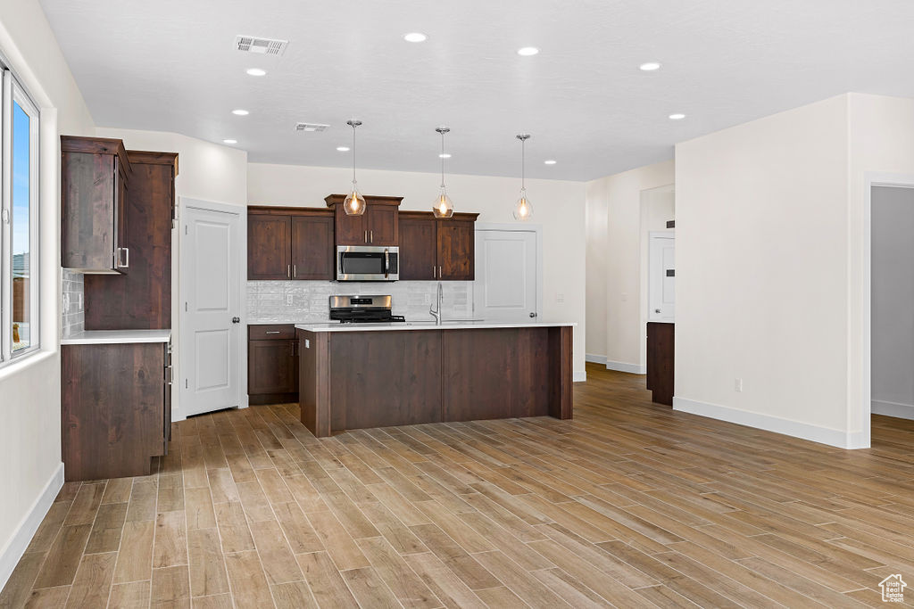 Kitchen with pendant lighting, backsplash, range, and light hardwood / wood-style floors
