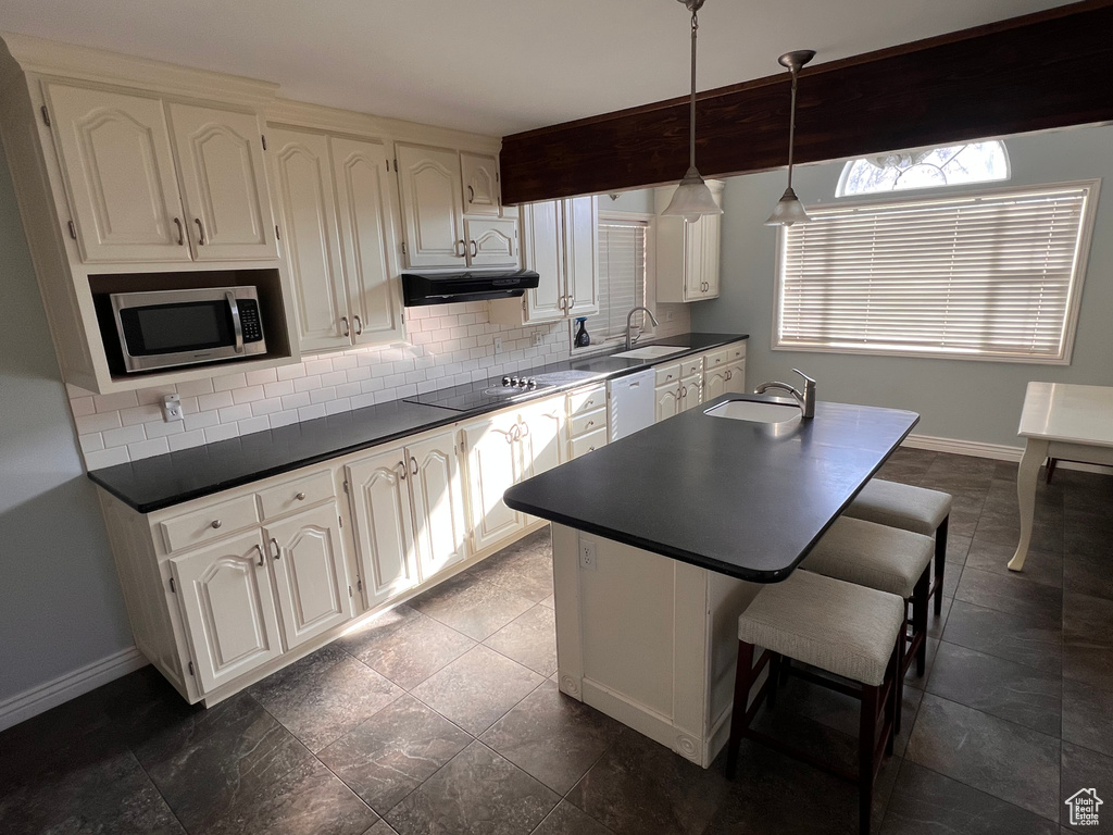 Kitchen with a breakfast bar area, backsplash, dark tile flooring, decorative light fixtures, and white cabinetry